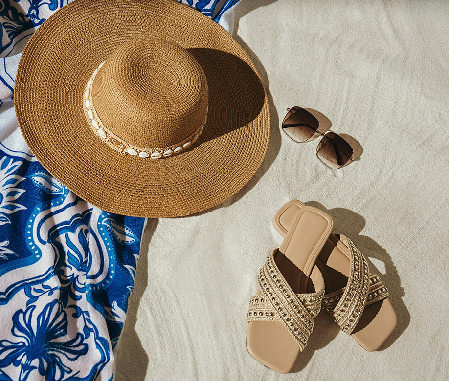 Sombrero, gafas y sandalias sobre arena de playa de la marca Studio F