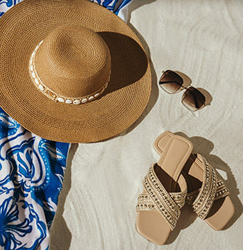 Sombrero, gafas y sandalias sobre arena de playa de la marca Studio F