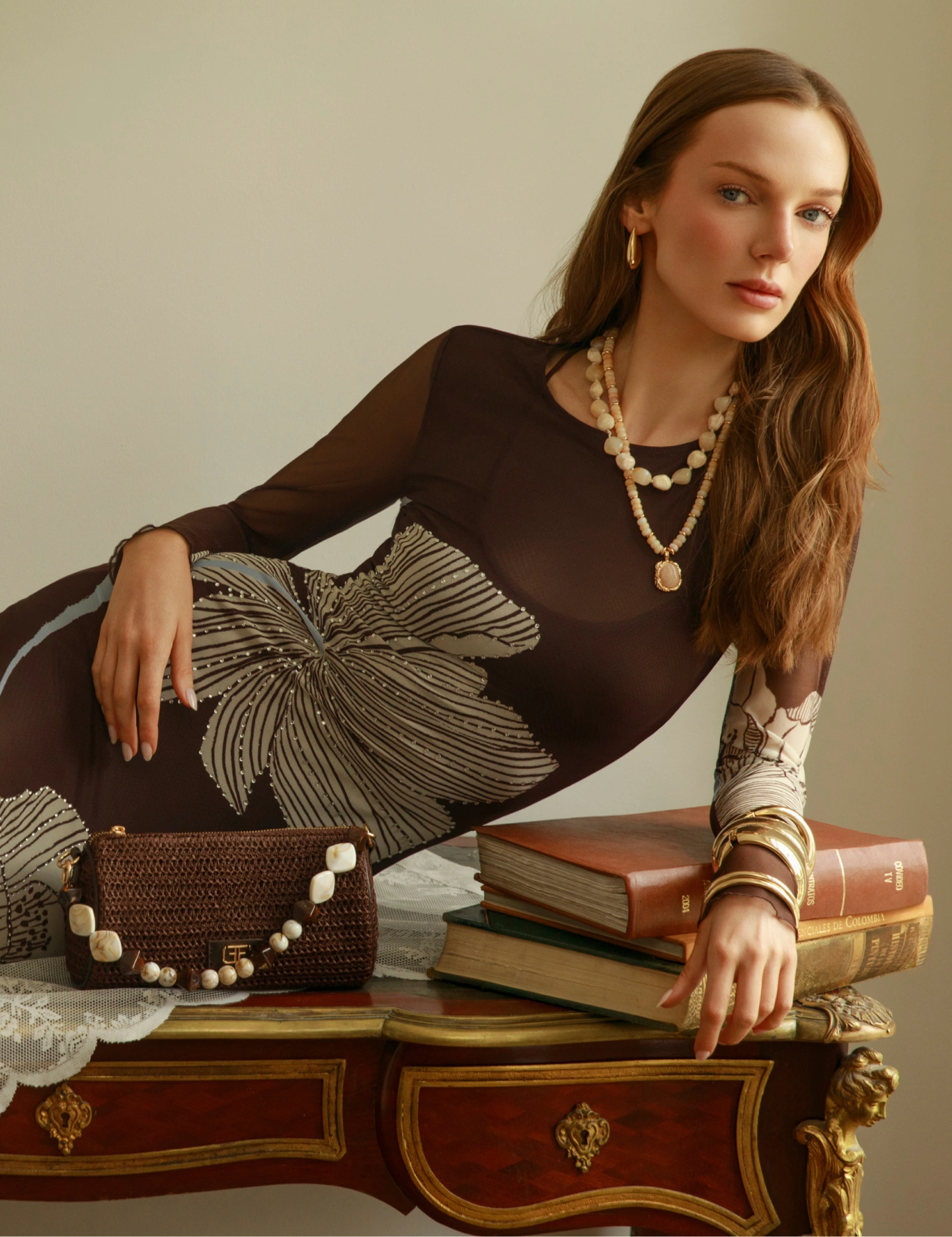 Look café con bordado floral | Legado Studio F Mujer con blusa café semitransparente de manga larga y prenda inferior con gran bordado floral en tonos beige, acompañada de collares dorados.