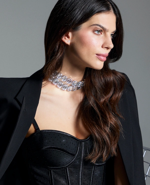 Modelo con collar plateado llamativo, blazer negro y top negro para complementar un look de noche.