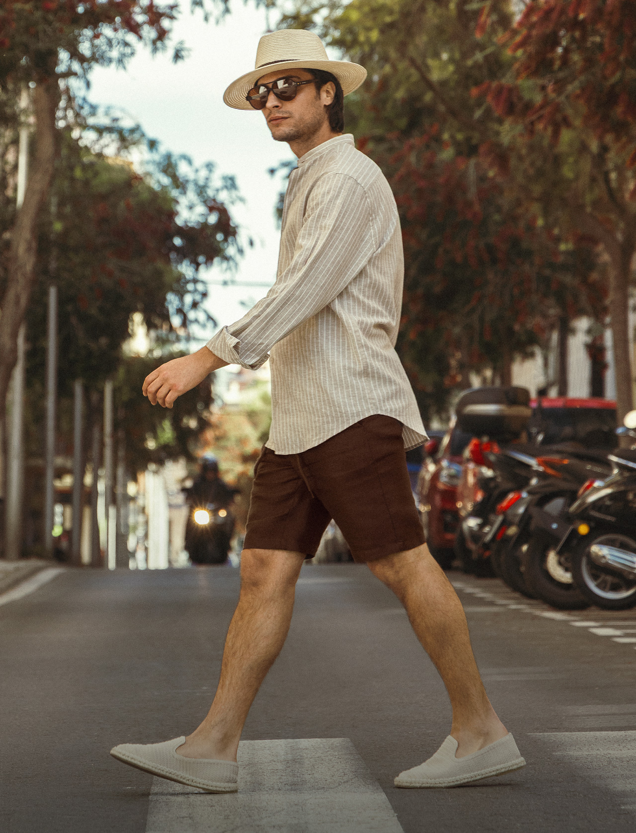 Hombre luciendo bermuda café, zapatos cerrados casuales, camisa manga larga, gafas de sol y sombrero