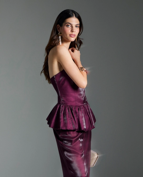 Modelo con blusa strapless vinotinto con detalle peplum y acabado brillante, combinada con pantalón a tono.
