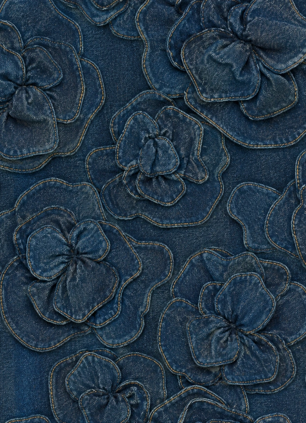 Foto de acercamiento del tejido denim azul decorado con flores en relieve y costuras visibles en tonos contrastantes.