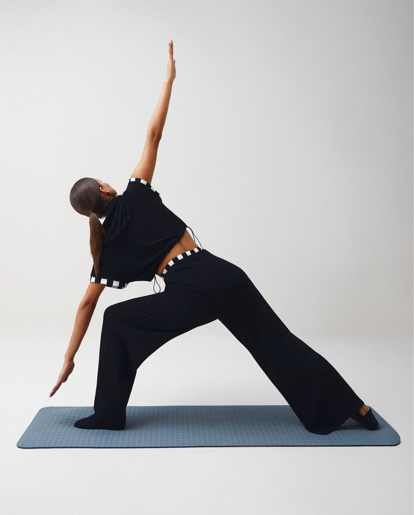 Mujer practicando yoga con ropa deportiva femenina, pantalón deportivo y top cómodo en color negro de la marca studio f