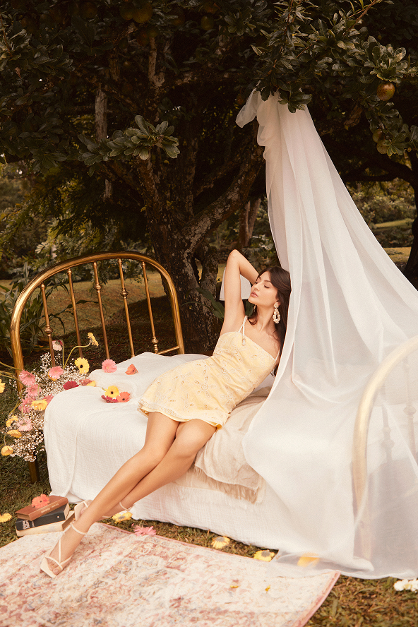 Modelo sobre una cama, usando vestido amarillo corto de Studio F.  Look romántico de primavera.